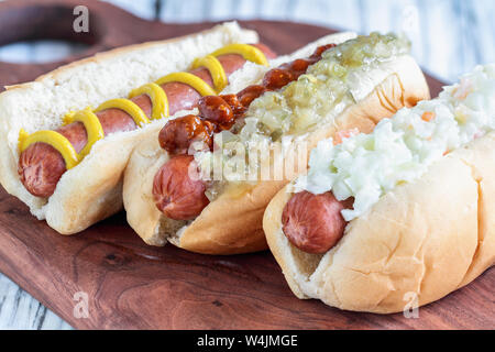 Trois variétés de hot dog sur une planche à découper. Avec une salade de chou, une avec relish pickle et un piment et une plaine avec de la moutarde. Selective Banque D'Images