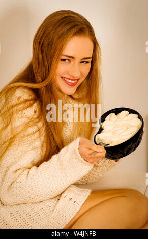 Smiling woman eating ice cream assis sur un canapé dans la maison. Elle triche sur l'alimentation. Banque D'Images