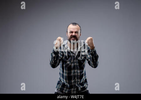 L'homme en colère de grincer ses dents et ses poings balling comme il se penche vers la caméra avec une expression vindicative, isolé sur gray with copy space Banque D'Images