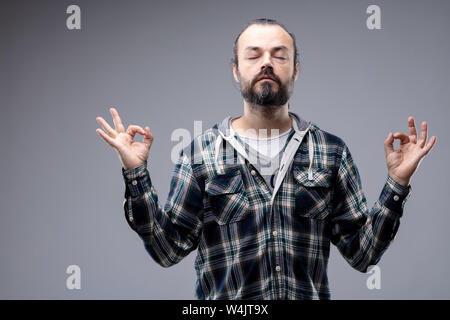 Homme barbu méditer avec une expression sereine et les yeux fermés alors qu'il bénéficie d'un moment de calme de concentration spirituelle, isolé sur le gris avec spa de copie Banque D'Images