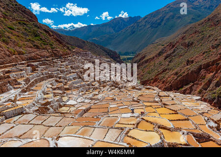 Terrasses de sel de Maras près de Cusco avec méconnaissable touristes entre les étangs de sel marche et les sommets enneigés des Andes, crête de montagne Salkantay au Pérou. Banque D'Images