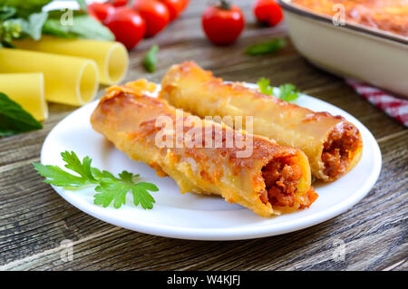 Cannelloni farcis avec de la sauce béchamel. Cuit pâtes cannelloni à la viande, sauce crème, fromage sur un fond de bois. Banque D'Images