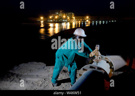 Exploitation minière, gestion et transport des sables bitumineux en titane. Superviseur de l'usine à la vanne de contrôle de nuit sur la tuyauterie vers l'usine de concentration humide (WCP) derrière Banque D'Images