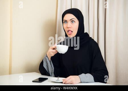 Femme musulmane de faire drôle de visage tout en buvant du café à la maison Banque D'Images