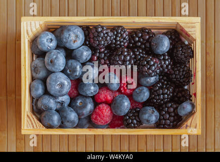 Les dons de la nature. Les framboises, les cerises, les bleuets, et les mûres dans une petite cage sur un tapis. Banque D'Images