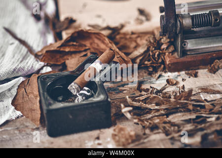 Close up d'un cigare cubain et un cendrier en céramique noire sur la table en bois séché et traité avec des feuilles de tabac. Banque D'Images