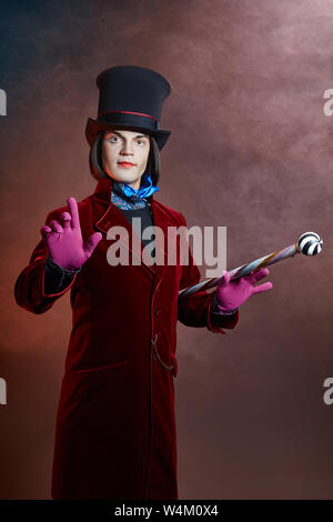 L'homme cirque fabuleux dans un chapeau et un costume rouge posant dans la fumée de couleur sur un fond sombre. Un clown lors d'une fête, l'homme représentant d'un conte de fées. Wiz Banque D'Images