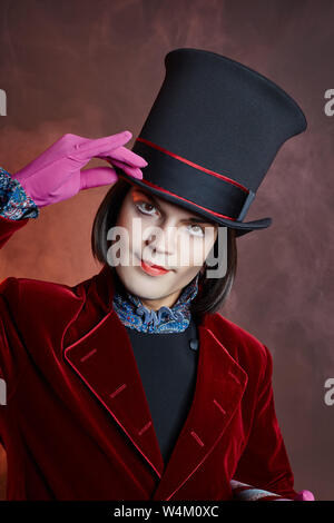 L'homme cirque fabuleux dans un chapeau et un costume rouge posant dans la fumée de couleur sur un fond sombre. Un clown lors d'une fête, l'homme représentant d'un conte de fées. Wiz Banque D'Images