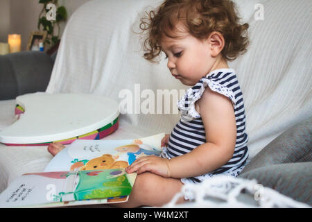 Petite fille lisant un livre d'images sur un canapé blanc Banque D'Images