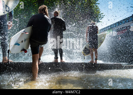 Munich, Allemagne. 24 juillet, 2019. Les surfeurs sont debout dans le jet d'eau d'un surfer au bord de l'Eisbach vague dans le jardin anglais. La vague est un hotspot populaires pour les surfeurs toute l'année. L'Allemagne est confrontée à une vague de chaleur - et déjà le Mercredi ce sera clairement visible dans de nombreux domaines. Crédit : Peter Kneffel/dpa/Alamy Live News Banque D'Images