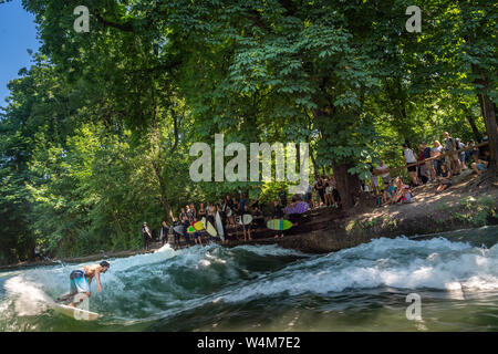 Munich, Allemagne. 24 juillet, 2019. Les surfeurs et les spectateurs sont au bord de l'Eisbach vague dans le jardin anglais, tandis qu'un autre internaute est sur l'eau. La vague est un hotspot populaires pour les surfeurs toute l'année. L'Allemagne est confrontée à une vague de chaleur - et déjà le Mercredi ce sera clairement visible dans de nombreux domaines. Crédit : Peter Kneffel/dpa/Alamy Live News Banque D'Images