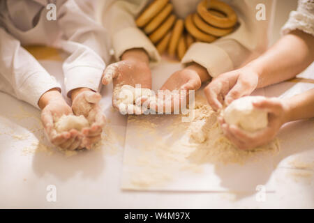 Mains close-up avec la pâte et la farine, heureux petits enfants sous la forme d'un chef pour cuisiner un délicieux Banque D'Images