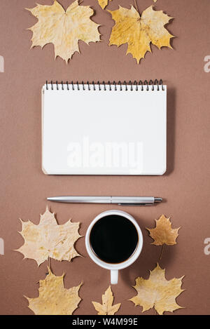 Espace de travail avec feuilles d'érable dorées, tasse de café, des bosses, carnet et un stylo sur fond brun. La composition créative. Automne ou Hiver concept. Mise à plat, Banque D'Images