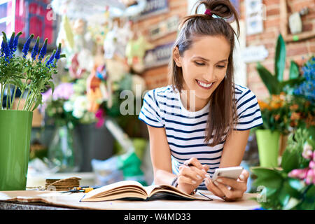 Photo de cheerful florist looking at tablet compteur dans sa boutique Banque D'Images