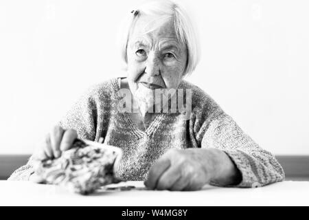 Concernés femme âgée assise à la table en comptant l'argent dans son portefeuille. Photo en noir et blanc. Banque D'Images