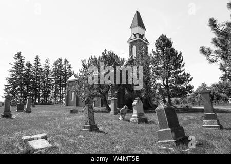 Pays abandonner Grave yard avec ancienne église avec de vieux et tumestones femme priant et en rendant hommage à ses secouristes à sur ses genoux dans le culte. Banque D'Images