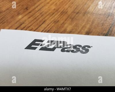 Close-up de logo pour péage automatisé agence E-ZPass, desservant le nord-est des États-Unis, sur un papier blanc contre une surface en bois clair, le 7 juillet 2019. () Banque D'Images