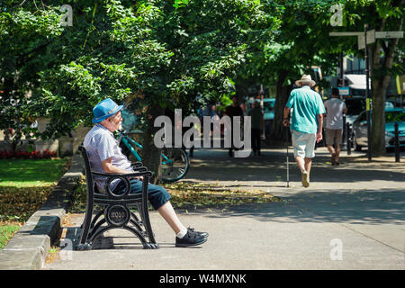 Un ancien senior man sitting on a bench sur une chaude journée d'été, de fumer sa pipe sur la Promenade Cheltenham Banque D'Images