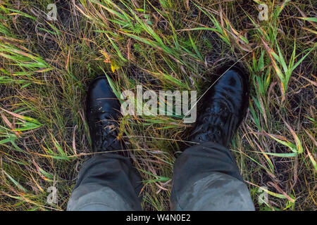 Les jambes dans des bottes militaires noir et vert pantalon de coton dans l'herbe d'automne vers le bas gonzo première personne. Banque D'Images