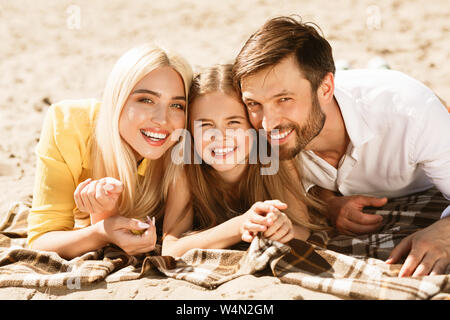 Heureux parents et fille lying together on picnic blanket Banque D'Images