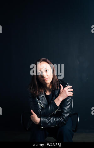 Studio portrait d'une belle jeune femme dans une veste en cuir noire contre un fond uni Banque D'Images