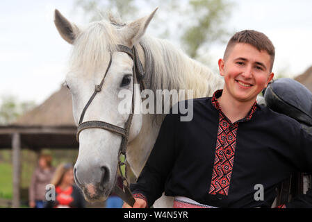 Petrikovka, région de Dniepropetrovsk, Ukraine, 28 04 2019 Un jeune homme, dans l'Ukraine cosaque brodé shirt sourit et est titulaire d'un cheval gris, ethniques festi Banque D'Images