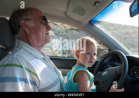 Boy driving car sur les grands-pères lap Banque D'Images