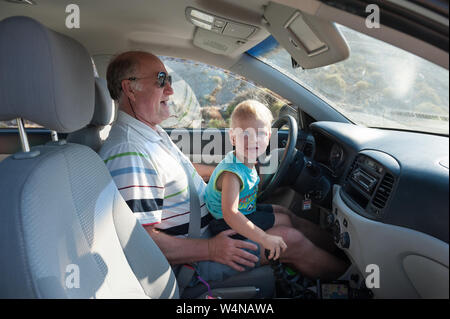 Boy driving car sur les grands-pères lap Banque D'Images