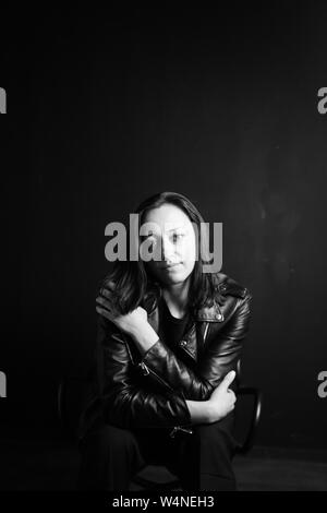 Studio portrait d'une belle jeune femme dans une veste en cuir noire contre un fond uni Banque D'Images