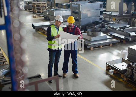 Vue de deux ingénieurs de l'uniforme et des casques parmi les équipements industriels de l'usine où ils travaillent, les deux plans d'entraide pro Banque D'Images