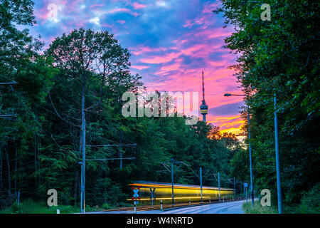 Allemagne, Stuttgart city tour de télévision en vert forêt avec ciel rougeoyant après le coucher du soleil à partir de la rue avec trafic tramway dans la belle nature paysage Banque D'Images