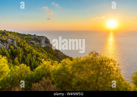 Grèce, Zante, coucher du soleil orange lumière sur l'océan bleu infini derrière les falaises rugueuses vert Banque D'Images