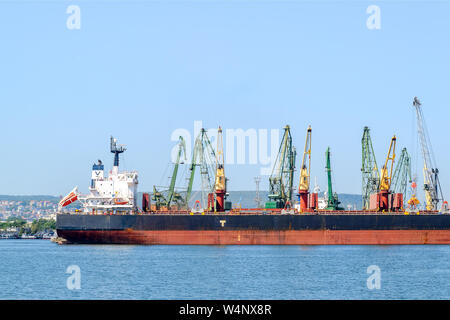 Varna, Bulgarie, le 22 juillet 2019. Grand cargo noir mer rouge tandis que le stationnement dans le port. Grues portuaires télécharger la cargaison dans le navire. Banque D'Images