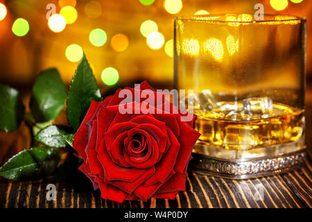 Verre de whisky écossais et de glace , rose rouge dans l'arrière-plan flou coloré de vacances sur table en bois Banque D'Images