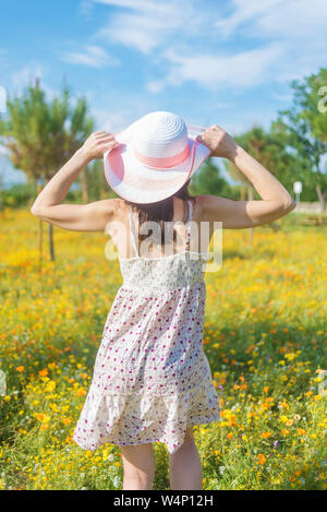 Vue arrière d'une femme en robe marche à travers un champ de fleurs tenant un chapeau Banque D'Images