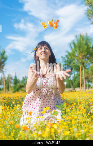 Belle femme en tenue d'assise sur un pré, tout en jetant des fleurs Banque D'Images