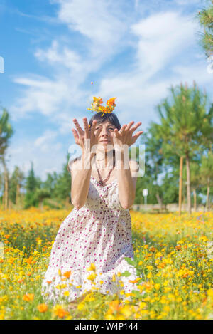 Belle femme en tenue d'assise sur un pré, tout en jetant des fleurs Banque D'Images