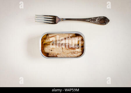 Les sardines en boîte et de la fourche sur la table rustique blanc fond