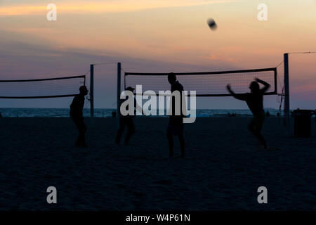 Silhouettes de quatre joueurs de volley-ball jouant sur la plage au coucher du soleil avec vue sur l'océan et un ciel coloré à l'arrière-plan. Huntington Beach, CA. Banque D'Images