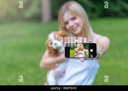 Portrait de belles femmes dans le parc, serrant avec l'épagneul chien et faire par téléphone intelligent selfies Banque D'Images