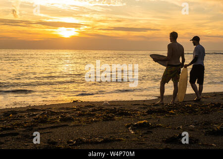 Aberystwyth, Pays de Galles, Royaume-Uni. 24 juillet 2019. Les jeunes hommes de l'embarquement sur les vagues sur la plage d'Aberystwyth au coucher du soleil sur une autre journée torride comme un panache d'air chaud continue à dériver en provenance du continent. Les températures devraient atteindre les 30 degrés Celsius dans certaines régions si le sud-est de l'UK le jeudi 25 juillet. Crédit photo Keith Morris / Alamy Live News Banque D'Images