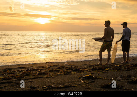 Aberystwyth, Pays de Galles, Royaume-Uni. 24 juillet 2019. Les jeunes hommes de l'embarquement sur les vagues sur la plage d'Aberystwyth au coucher du soleil sur une autre journée torride comme un panache d'air chaud continue à dériver en provenance du continent. Les températures devraient atteindre les 30 degrés Celsius dans certaines régions si le sud-est de l'UK le jeudi 25 juillet. Crédit photo Keith Morris / Alamy Live News Banque D'Images