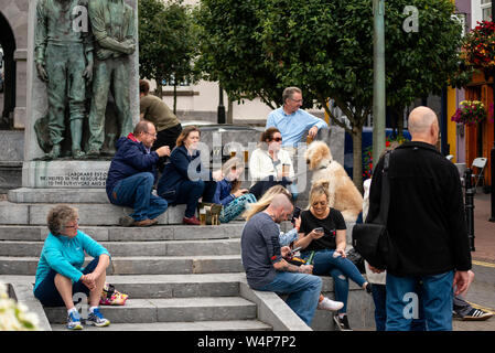 Les touristes dans la ville de Cobh Ireland vue des gens appréciant la fin de l'après-midi à la place Casement assis au Mémorial de Lusitania Banque D'Images