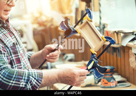 Carpenter Senior bateaux en bois d'encollage de surface et se joindre à l'aide de colliers. Menuisier bois avec de l'équipement et des outils à l'atelier. Meubles faits à la main Banque D'Images