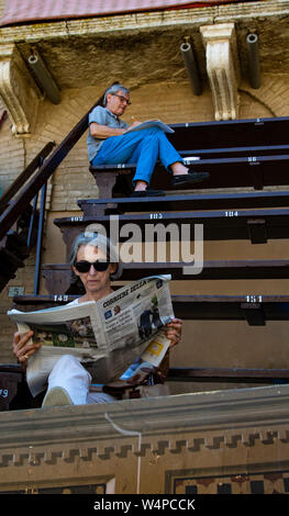 L'homme et de la femme lire les journaux dans les gradins sur la place de Campo en attendant le début de la Palio à Sienne, Italie Banque D'Images