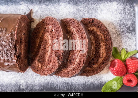 Swiss roll avec de la confiture au chocolat décoré avec des framboises dans une assiette. Des bonbons. Focus sélectif. Banque D'Images