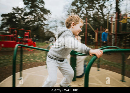 Vue latérale d'enfant sur merry go round à l'aire de jeux Banque D'Images