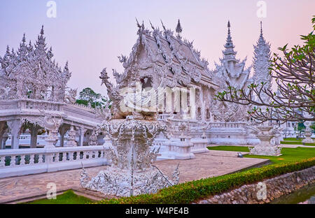 L'extérieur de l'Ubosot Temple blanc (bâtiment principal) avec grande sculpture de créature mythique, holding fleur de lotus dans la bouche, sur le premier plan, Chiang Ra Banque D'Images