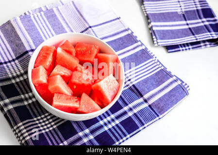 Bol avec des morceaux de pastèque rouge sur fond bleu, des serviettes sur fond blanc. Banque D'Images