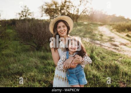 Portrait of happy young mother and daughter smiling in meadow rétroéclairé Banque D'Images